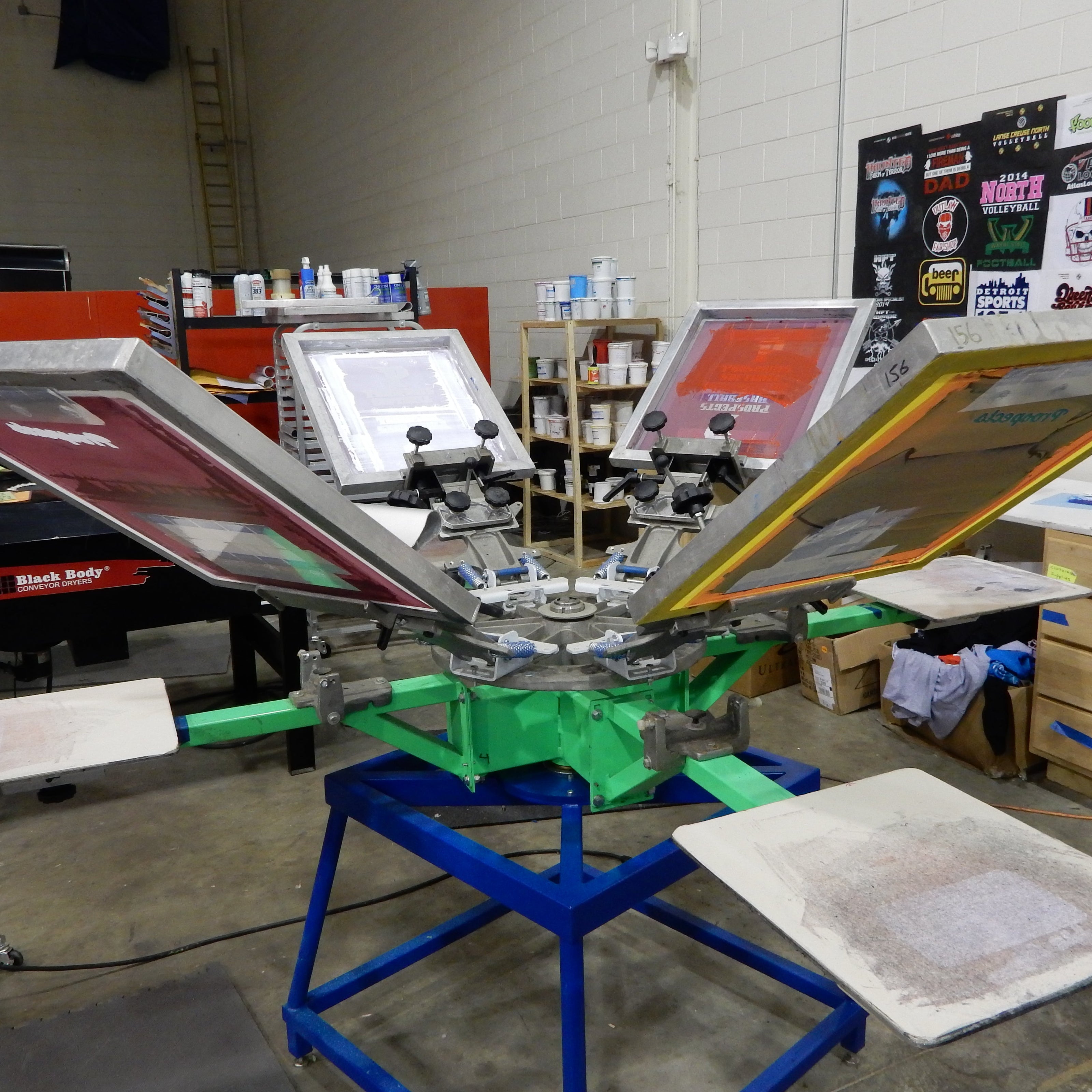 Screen printing press in a workshop with t-shirts hanging in the background